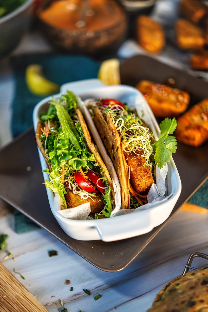 A plate of Asian tacos filled with lettuce, sprouts, and cherry tomatoes, garnished with a cilantro leaf.