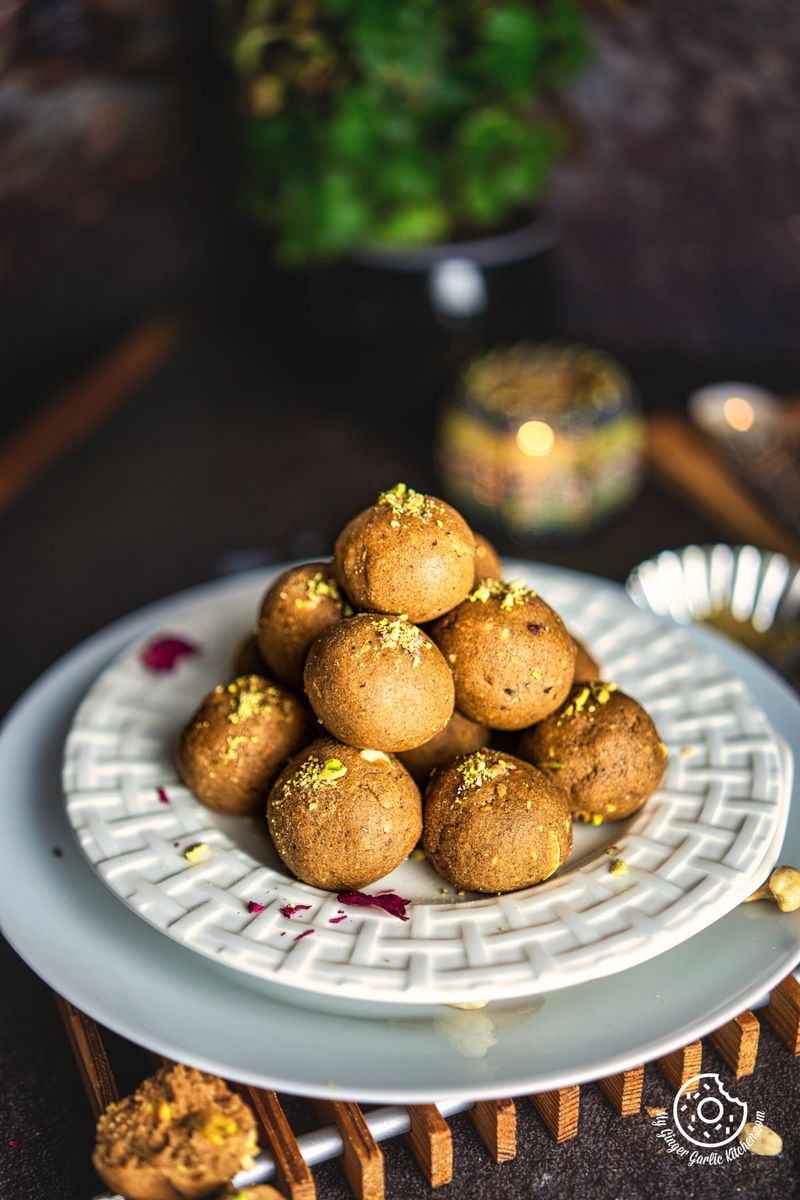 closeup of atta ladoo stacked in a white plate with a candle in the background