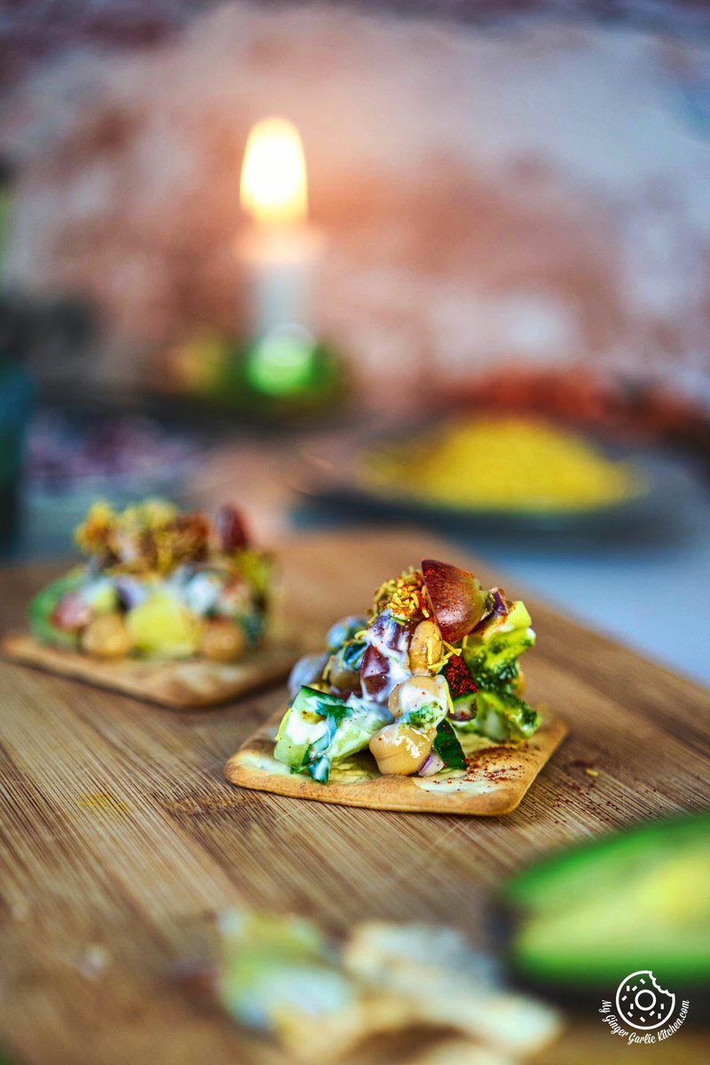 there are two small avocado chaat canapes on a wooden board with a candle in the background