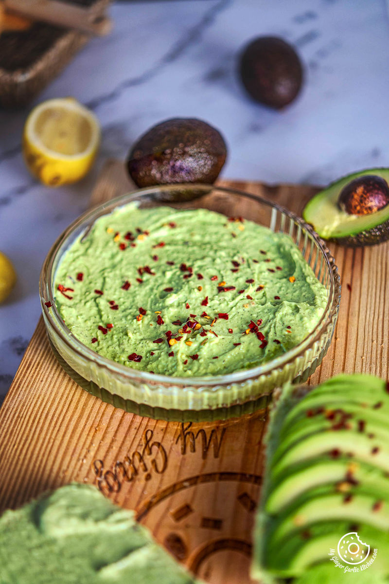 a bowl of avocado cheese spread on a cutting board with slices of avocado and lemons next to it