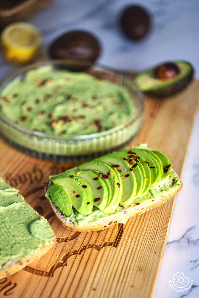 a slice of bread with avocado on it and a bowl avocado cheese spread next to it