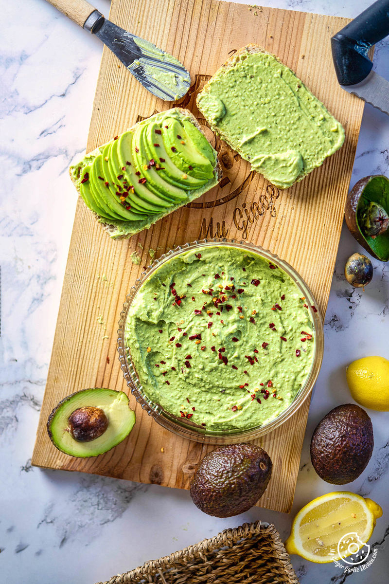 overhead photo of avocado dip on a wooden cutting board with lemons and avocados next to it
