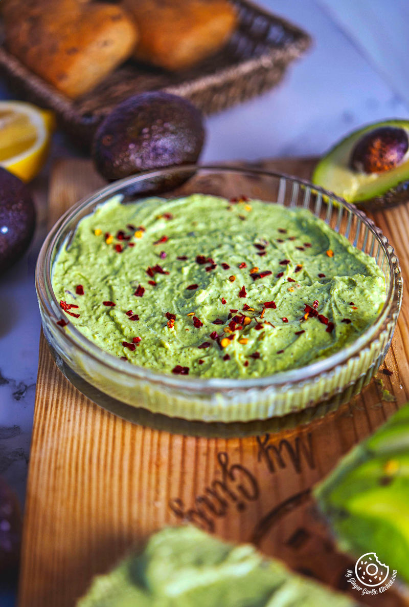 closeup photo of a bowl of avocado dip on a cutting board next to some bread, avocados and lemons