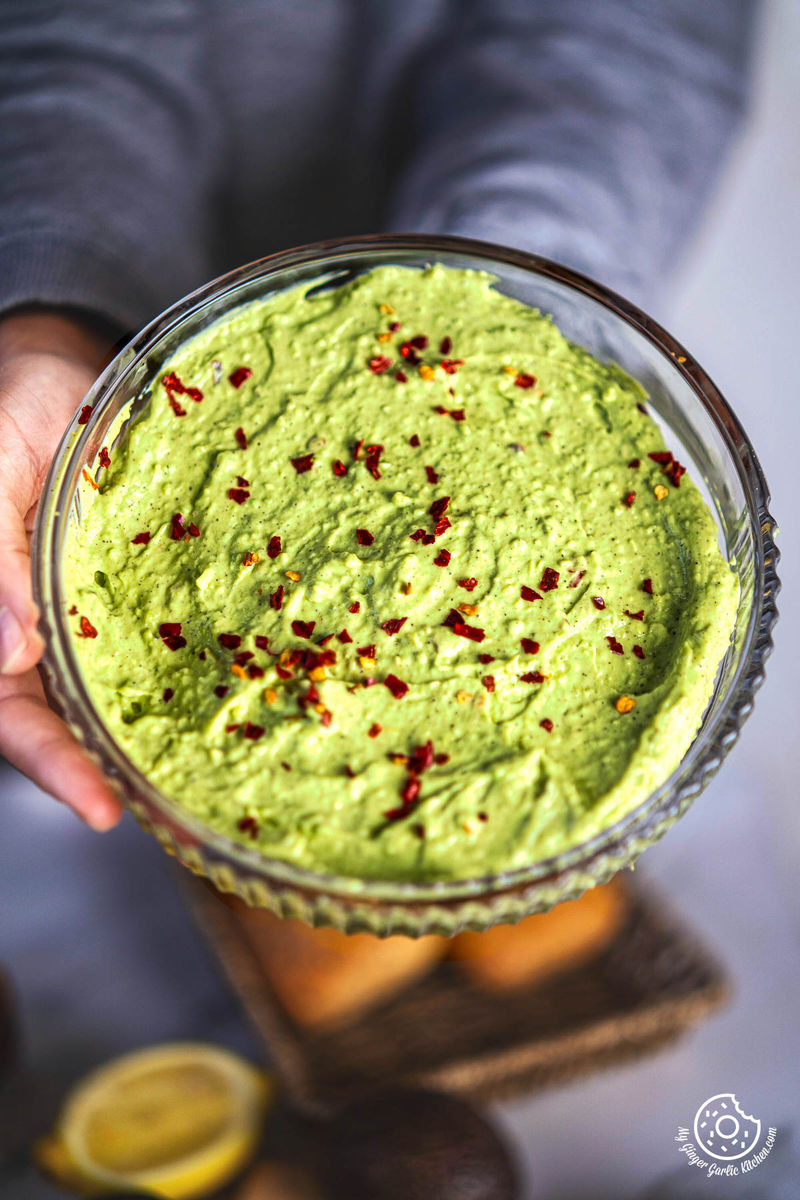 a person is spreading avocado cheese spread on a bread over wooden cutting board with lemons and avocados in the foreground