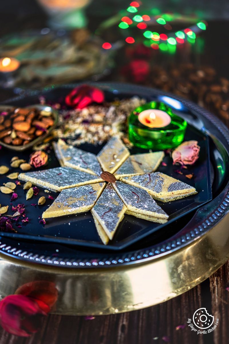 Badam Burfi decorated with silver leaf arranged as a flower shaped on a grey metal plate
