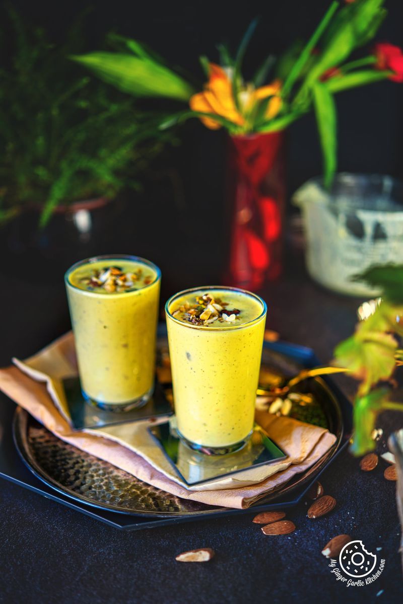 photo of two glasses of badam milkshake on a plate with flowers in the background