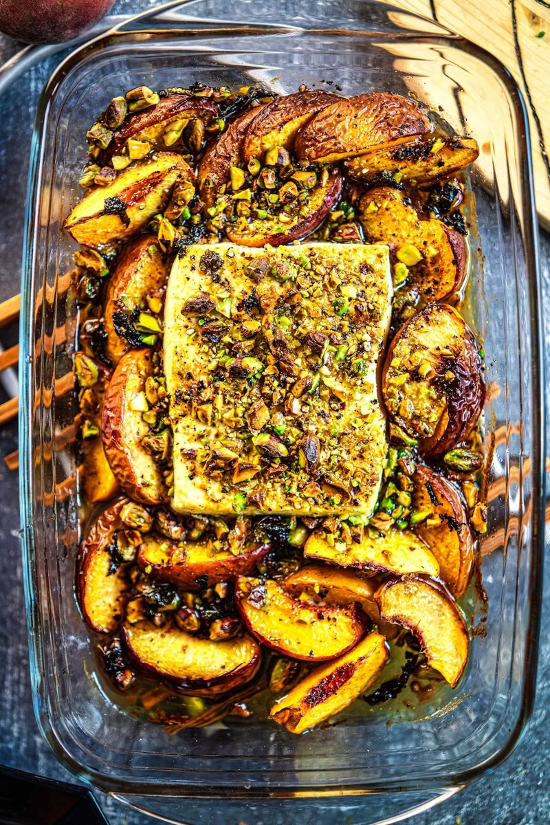 Baked peach feta with warm creamy feta, caramelized peach wedges, roasted pistachios, fresh mint, honey, and flavorful juices in a baking dish
