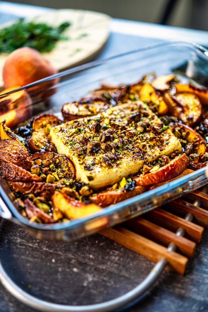 Close-up of baked peach feta with creamy feta, caramelized peaches, roasted pistachios, fresh mint, and honey served in a baking dish