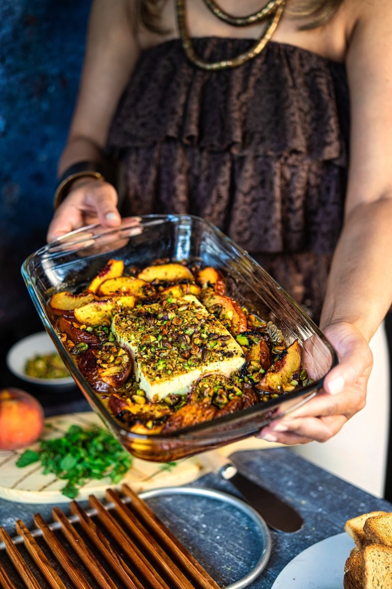 Baked peach feta served warm in a baking dish with caramelized peaches, creamy feta, pistachios, fresh mint, and honey