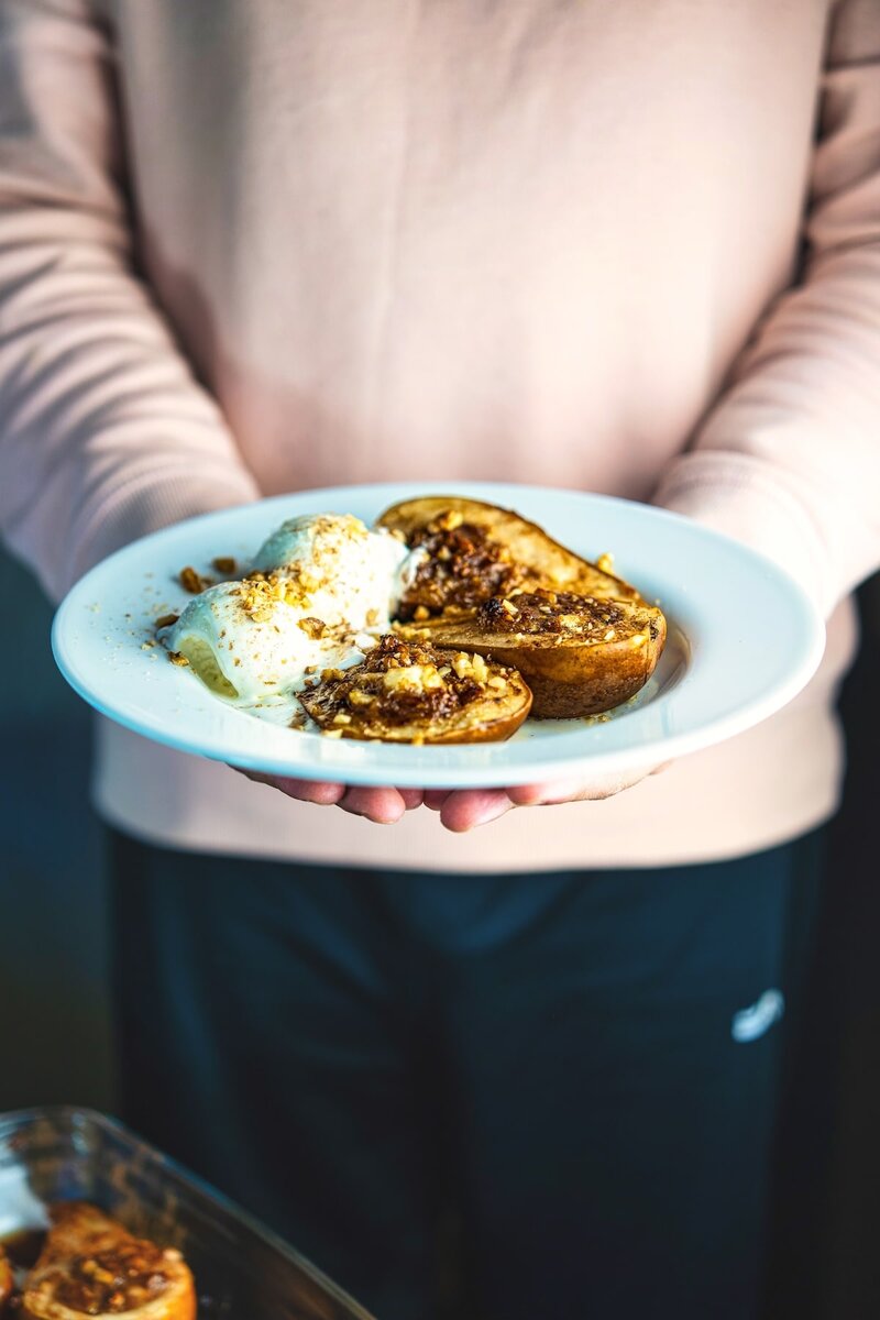 Baked pears with goat cheese and walnuts served warm with vanilla ice cream on a white plate, easy vegetarian dessert