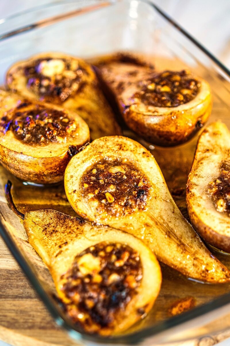 Close-up of baked pears filled with goat cheese, walnuts, cinnamon, and honey in a baking dish