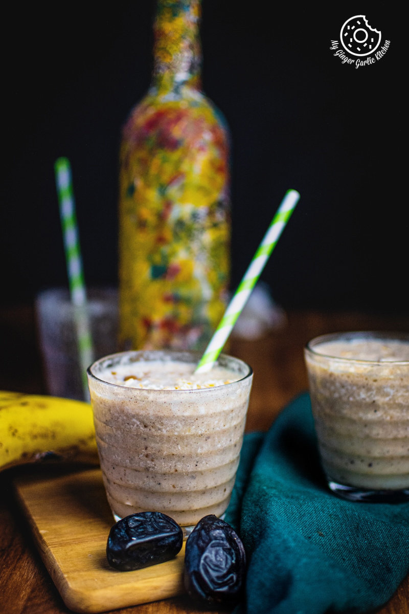 Banana date smoothies served in glasses, garnished with oats and cinnamon, accompanied by fresh bananas and dates.