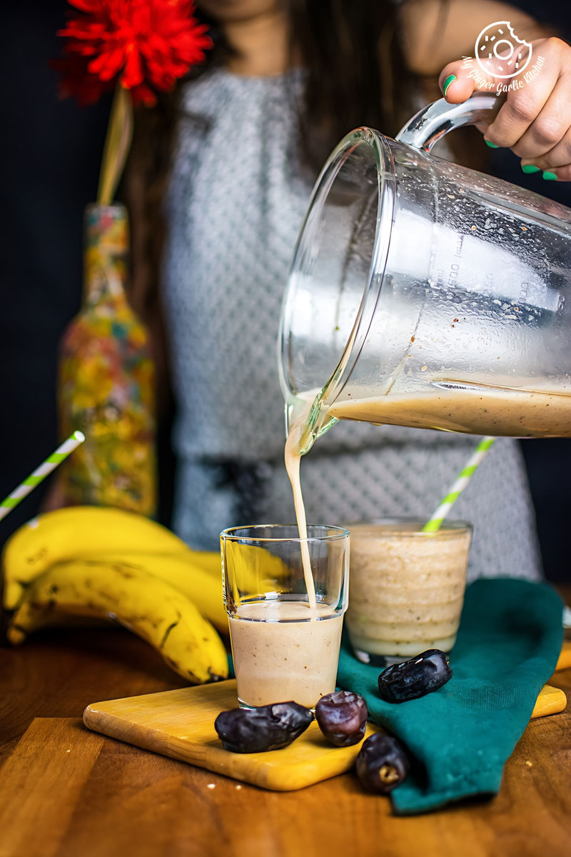 Woman pouring a rich banana date smoothie into a glass, with whole bananas and dates on the countertop.