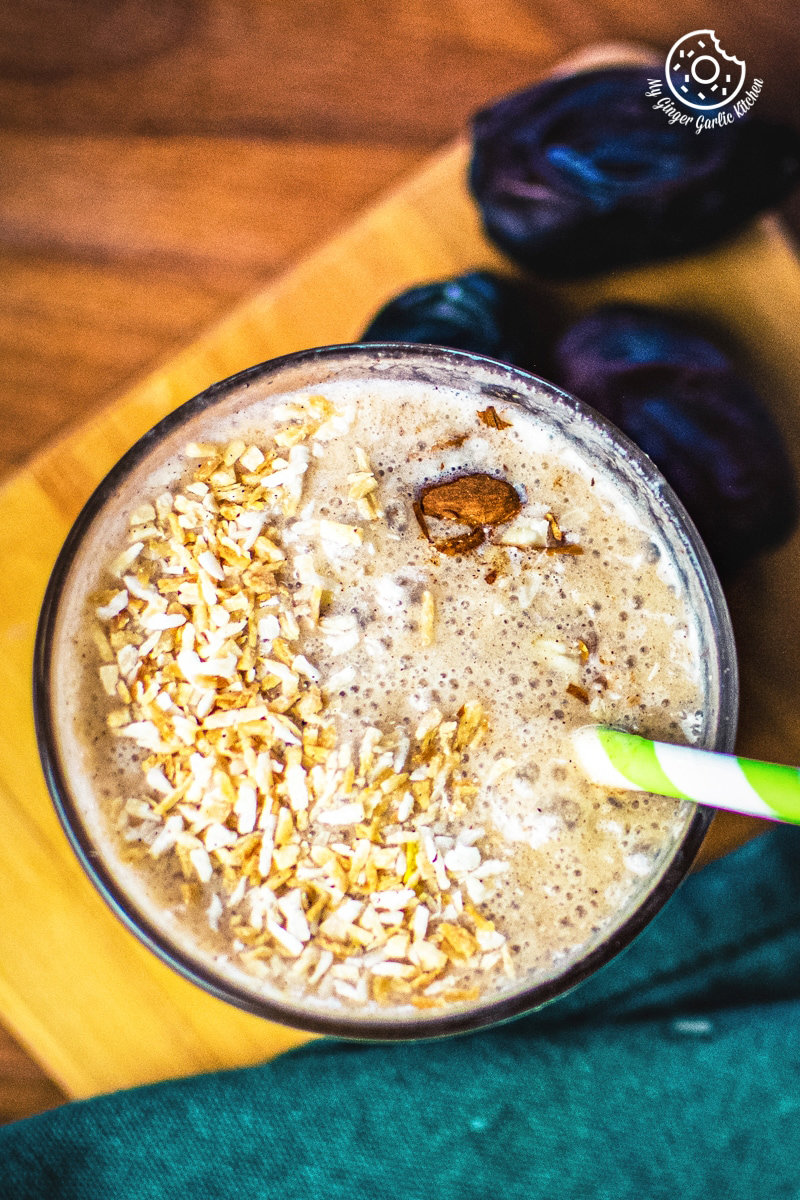 Top view of a thick banana date smoothie sprinkled with chopped nuts, a spoon inserted into the frothy mix.