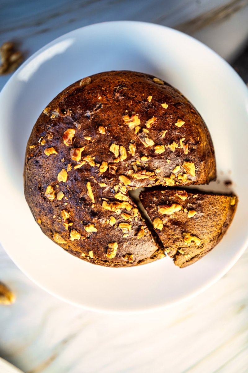 A top view of a banana date walnut cake with a single slice cut out, showcasing the walnut topping.