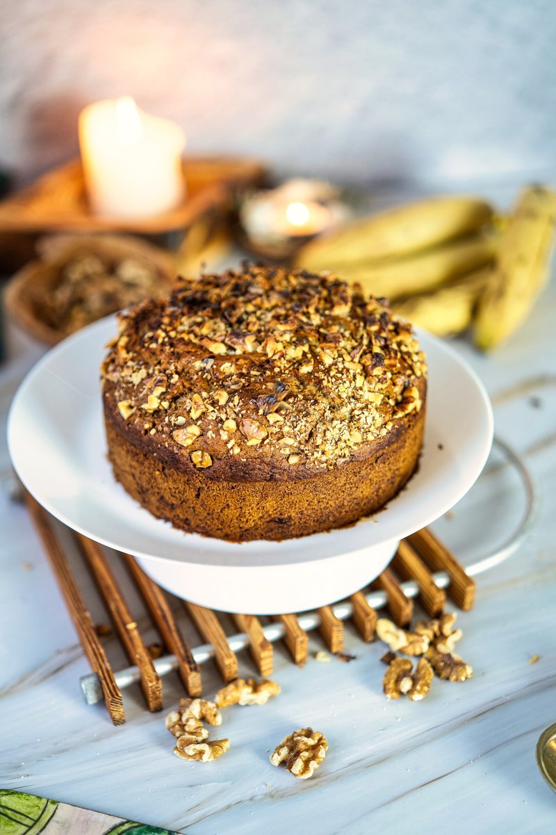 A freshly baked banana date walnut cake on a white plate, with bananas and walnuts in the background.