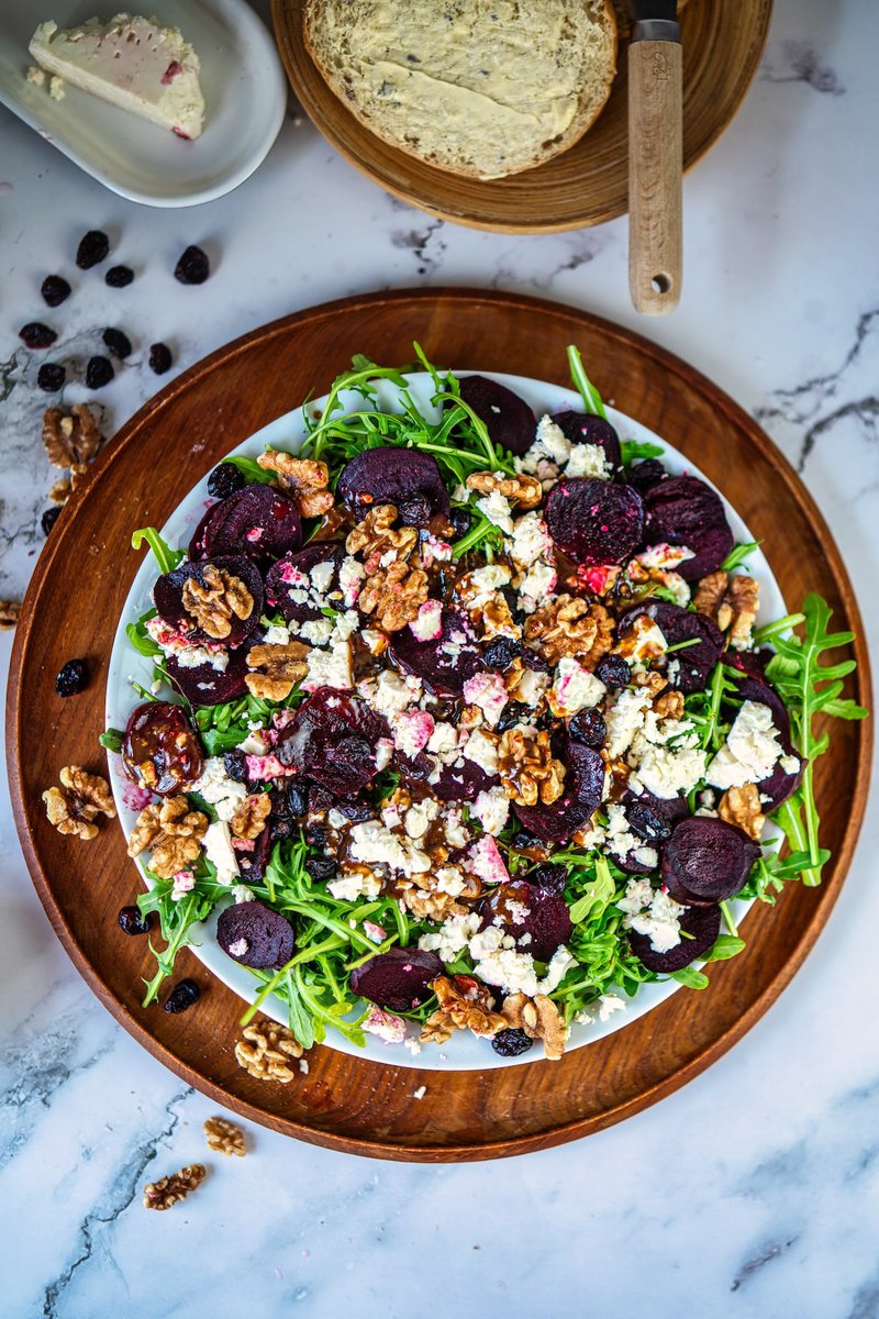 Fresh beetroot salad with arugula, walnuts, and goat cheese on a wooden platter, served with sliced bread and butter.