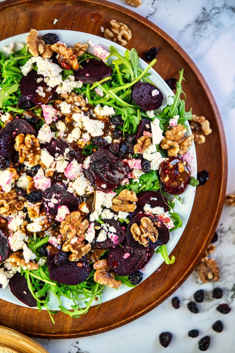 Close-up of a vibrant beetroot salad sprinkled with goat cheese and walnuts, with arugula leaves and dried cranberries.