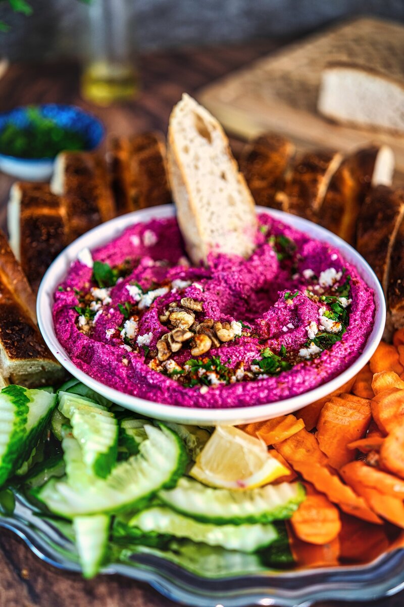 Beetroot walnut feta dip with a bread slice dipped in, served with cucumber, carrots, and toasted bread slices