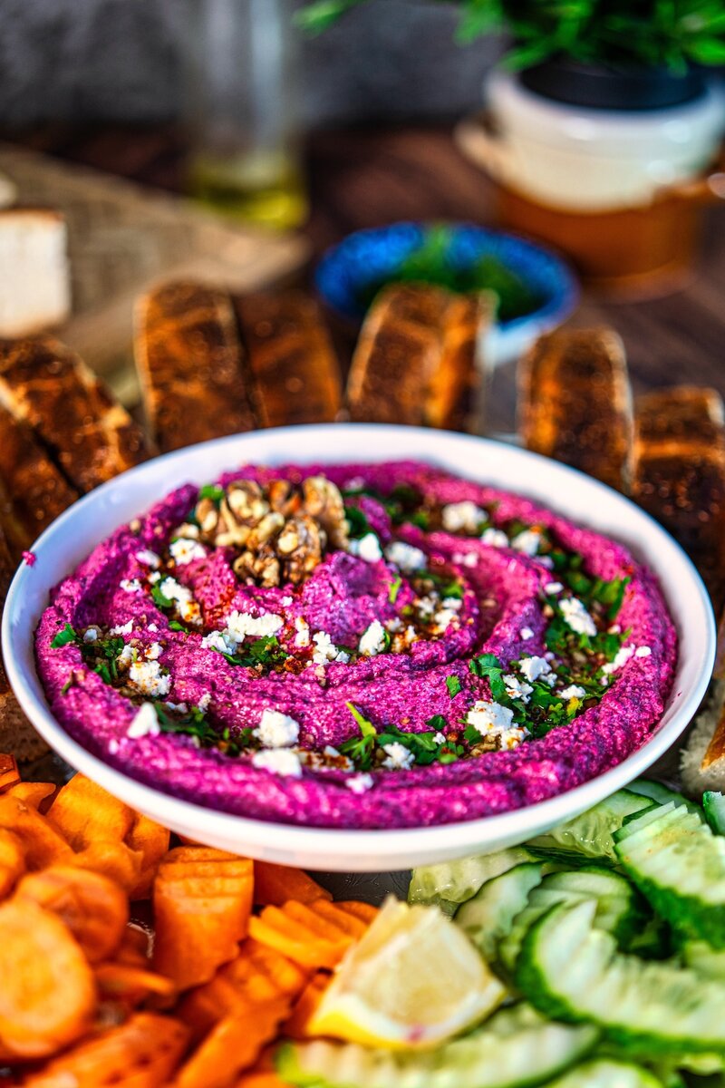 Beetroot walnut feta dip in a bowl topped with walnuts, feta, parsley, and olive oil served with bread and fresh vegetables