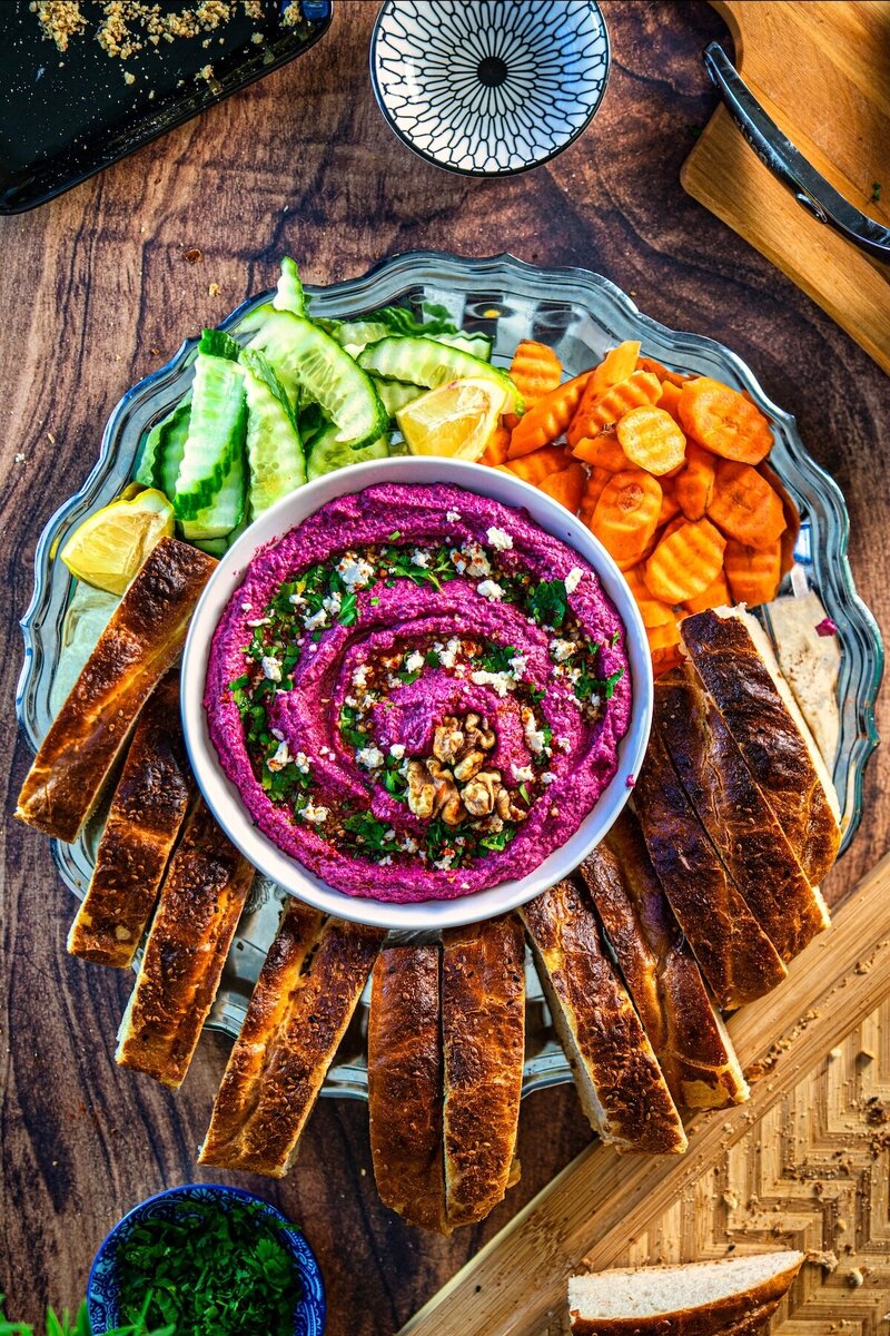 pTop view of creamy beetroot walnut feta dip platter with toasted bread, cucumber slices, carrots, and lemon wedges