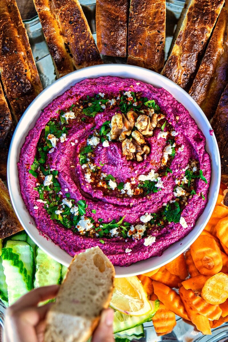 Close-up of vibrant beetroot walnut feta dip garnished with feta, herbs, and walnuts served with bread and veggies