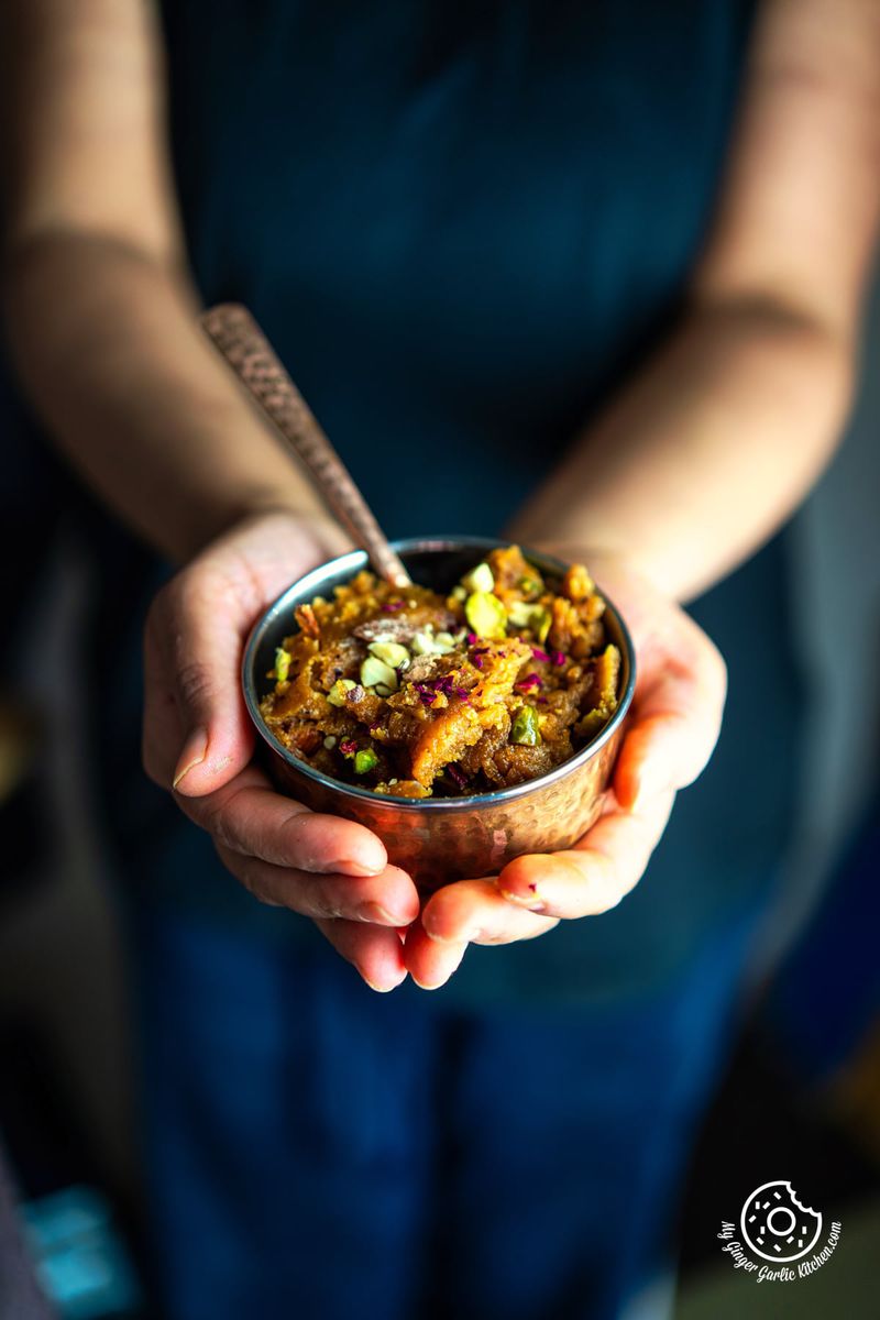 a female holding a copper bowl with besan halwa