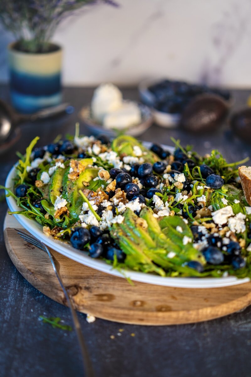 Blueberry avocado salad served on a wooden board with fresh greens, walnuts, and sliced bread on the side