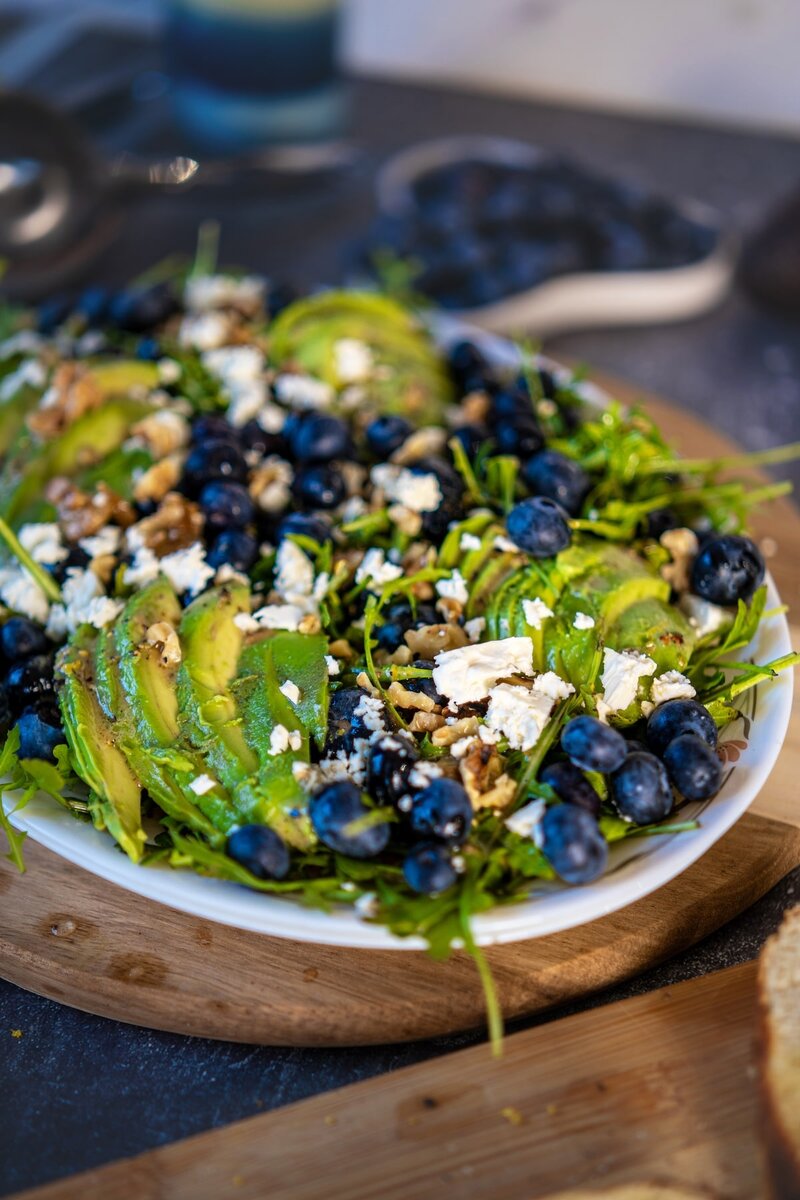 Close-up of blueberry avocado salad with sliced avocados, fresh blueberries, and crumbled vegan feta