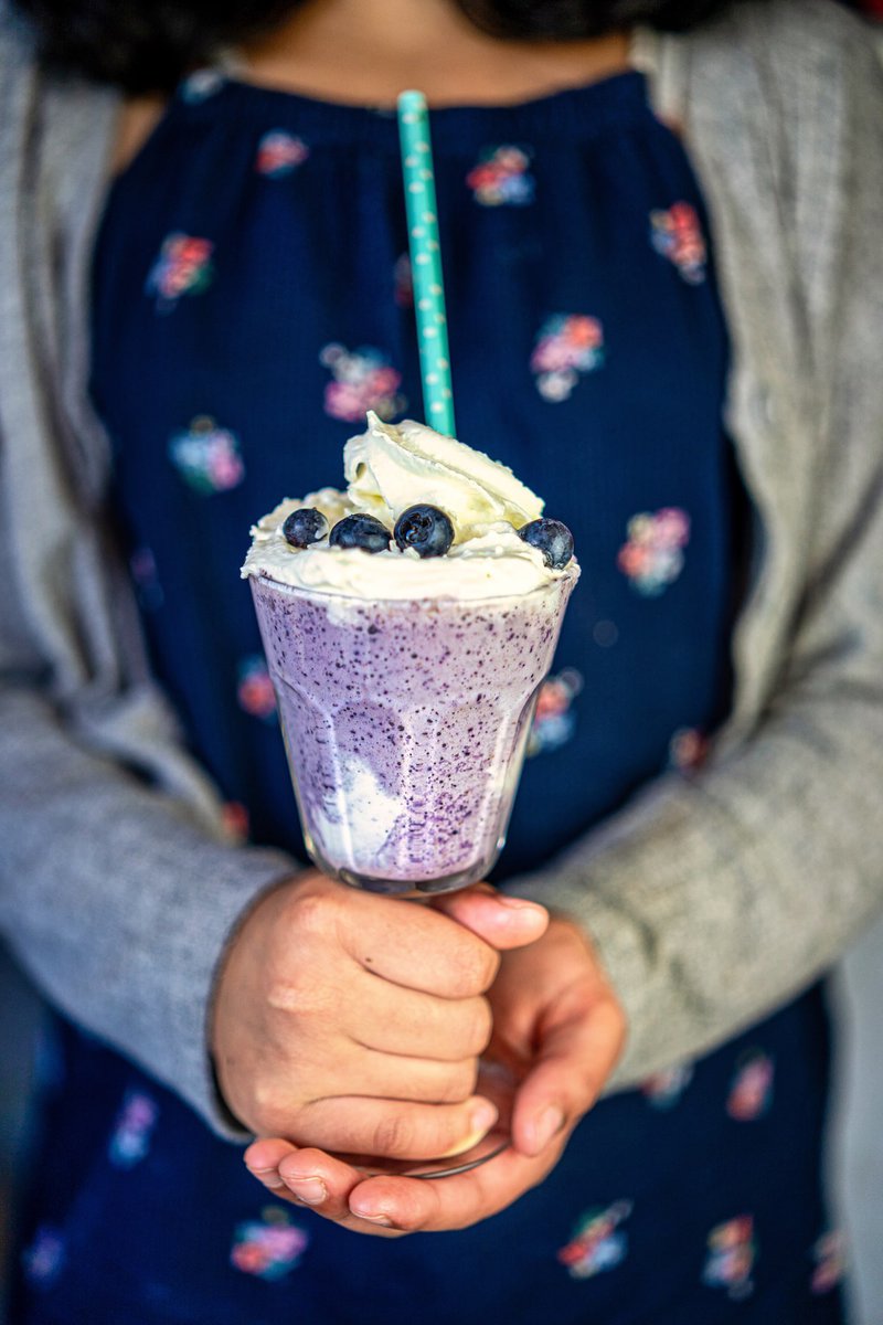 Person holding a blueberry milkshake topped with whipped cream and blueberries.