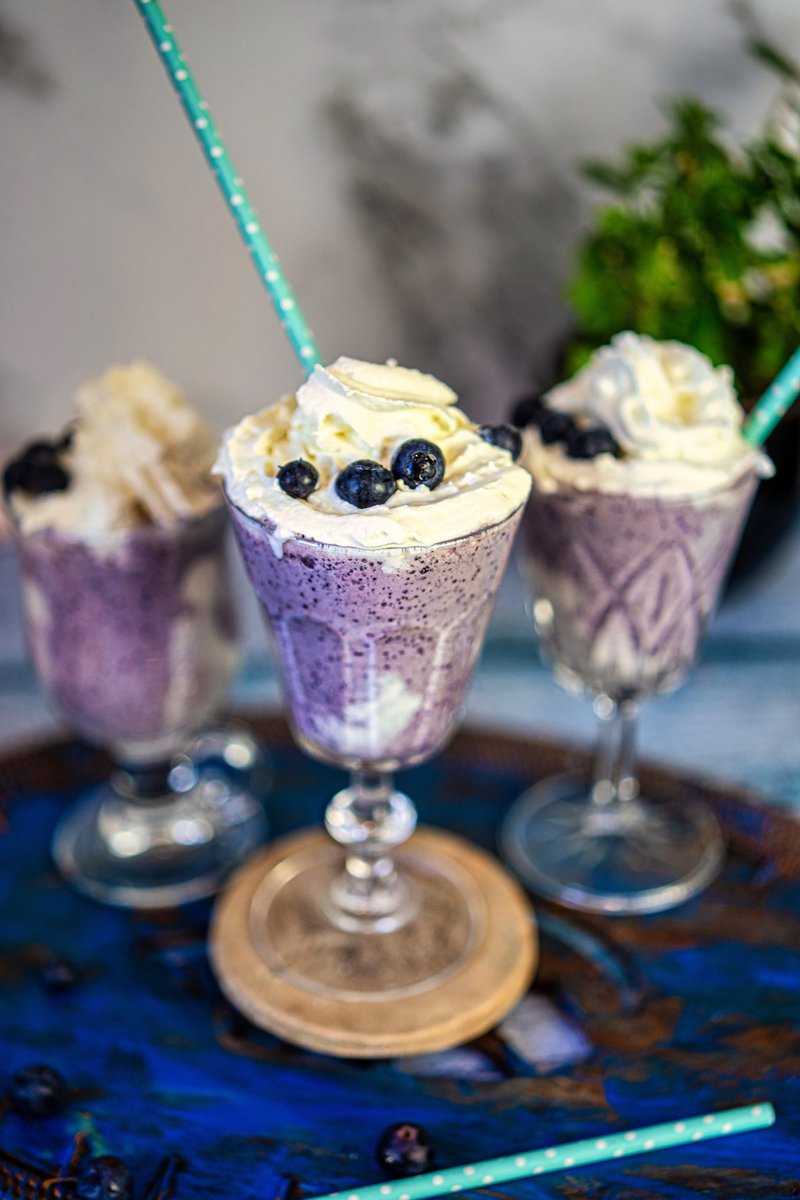 Three blueberry milkshakes served on a rustic tray, topped with whipped cream.