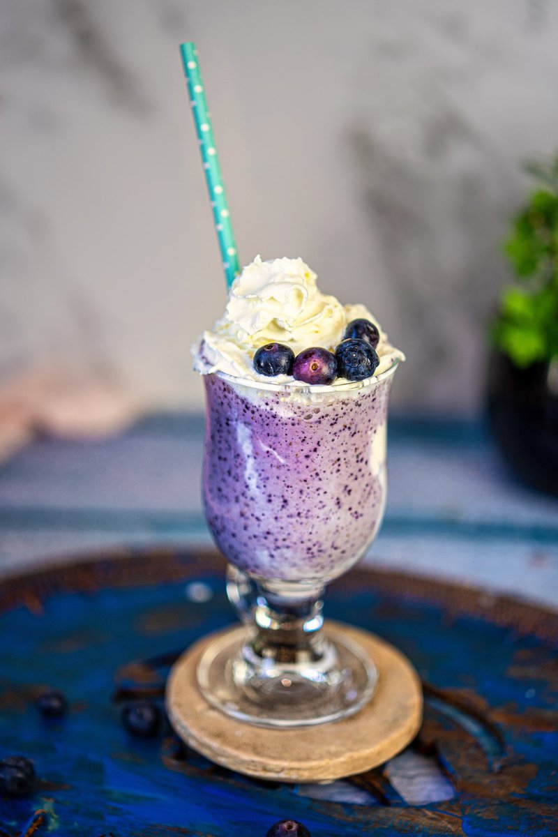 Close-up of a blueberry milkshake with whipped cream topping and a blue straw.