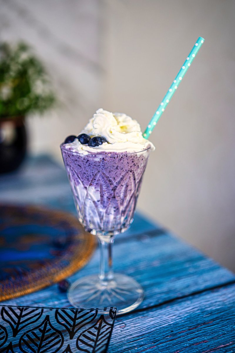 Elegant blueberry milkshake on a blue patterned table, garnished with whipped cream and blueberries.