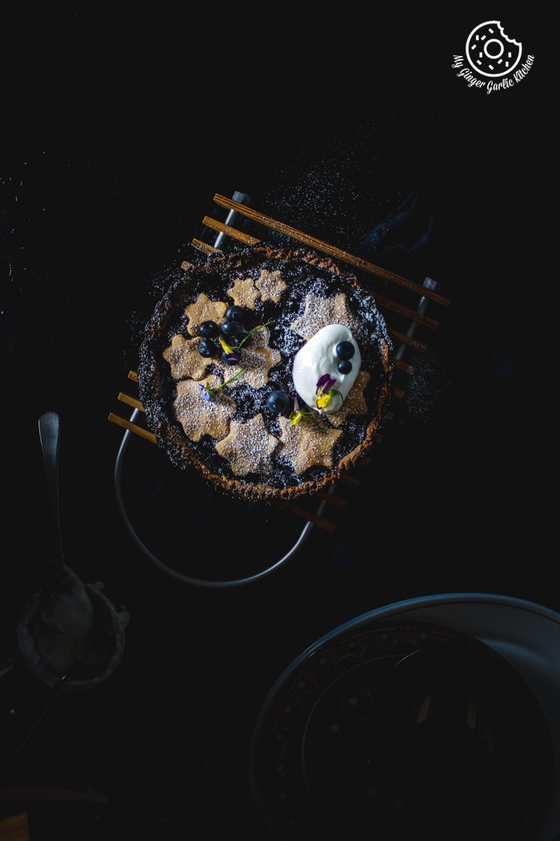 a blueberry pie with a scoop of sour cream and blueberries on top of it