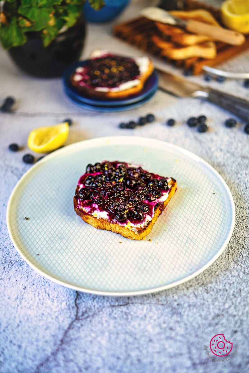 one blueberry toast in ceramic plate with one more toast and blueberries in the backgrouns
