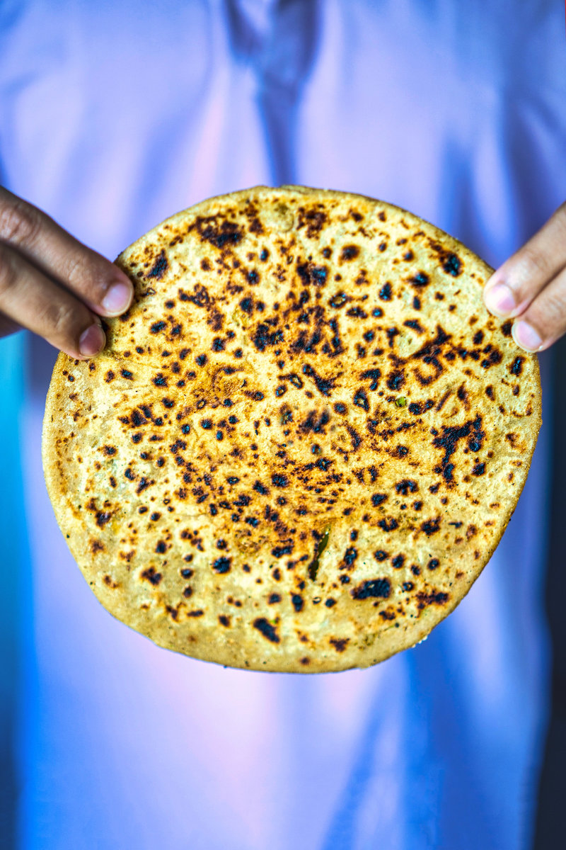 Person holding a broccoli paratha up to the camera, showcasing its texture and fillings.