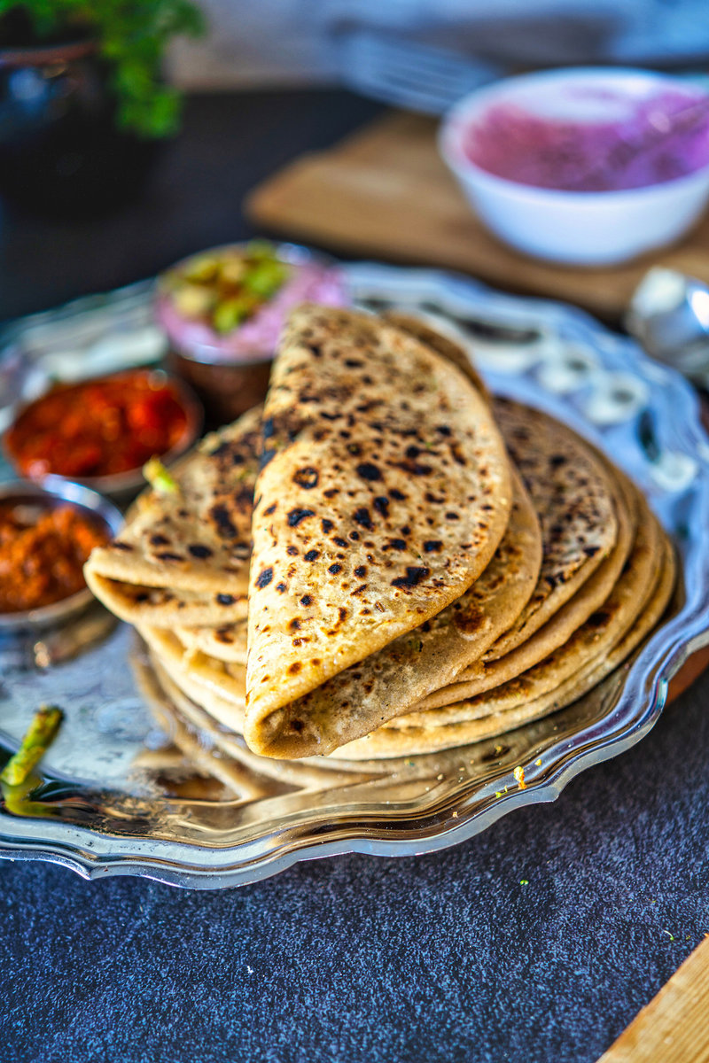 Folded broccoli parathas stacked on a decorative silver plate, garnished with a small piece of butter.