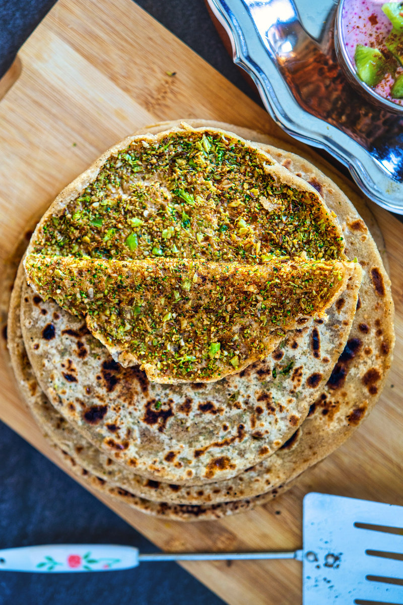 Close-up view of a broccoli paratha with visible broccoli and spice filling, served on a wooden cutting board.