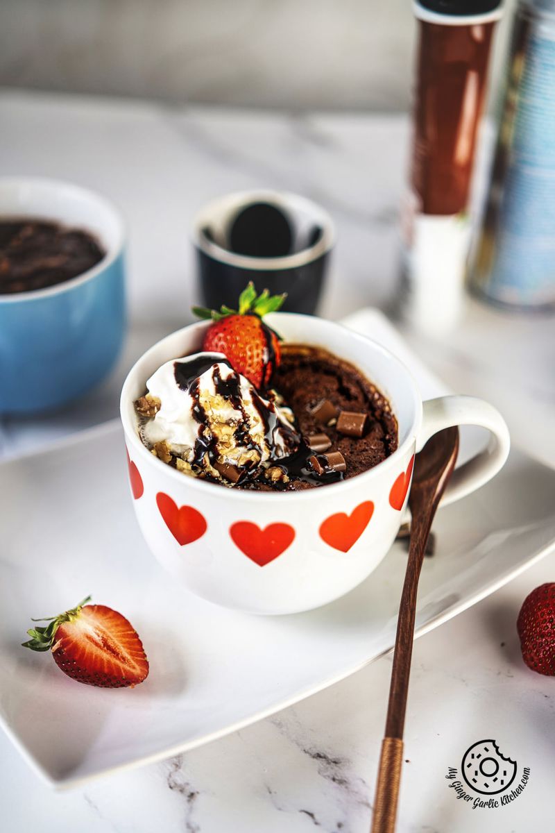 chocolate brownie in a white ceramic mug topped with whipped cream and strawberry
