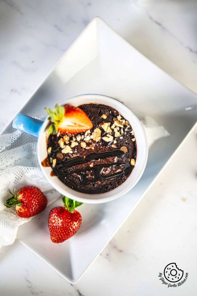 overhead shot of chocolate brownie in a blue ceramic mug topped with chopped walnuts and strawberry