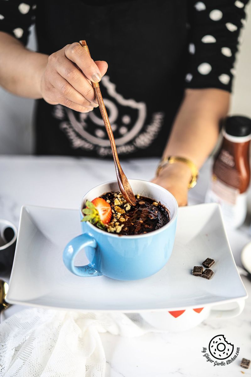 a female holding a wooden spoon over a chocolate brownie mug topped strawberry