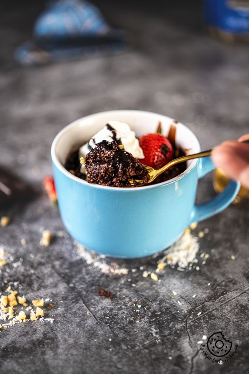 a hand holding a golden spoon over a chocolate brownie mug