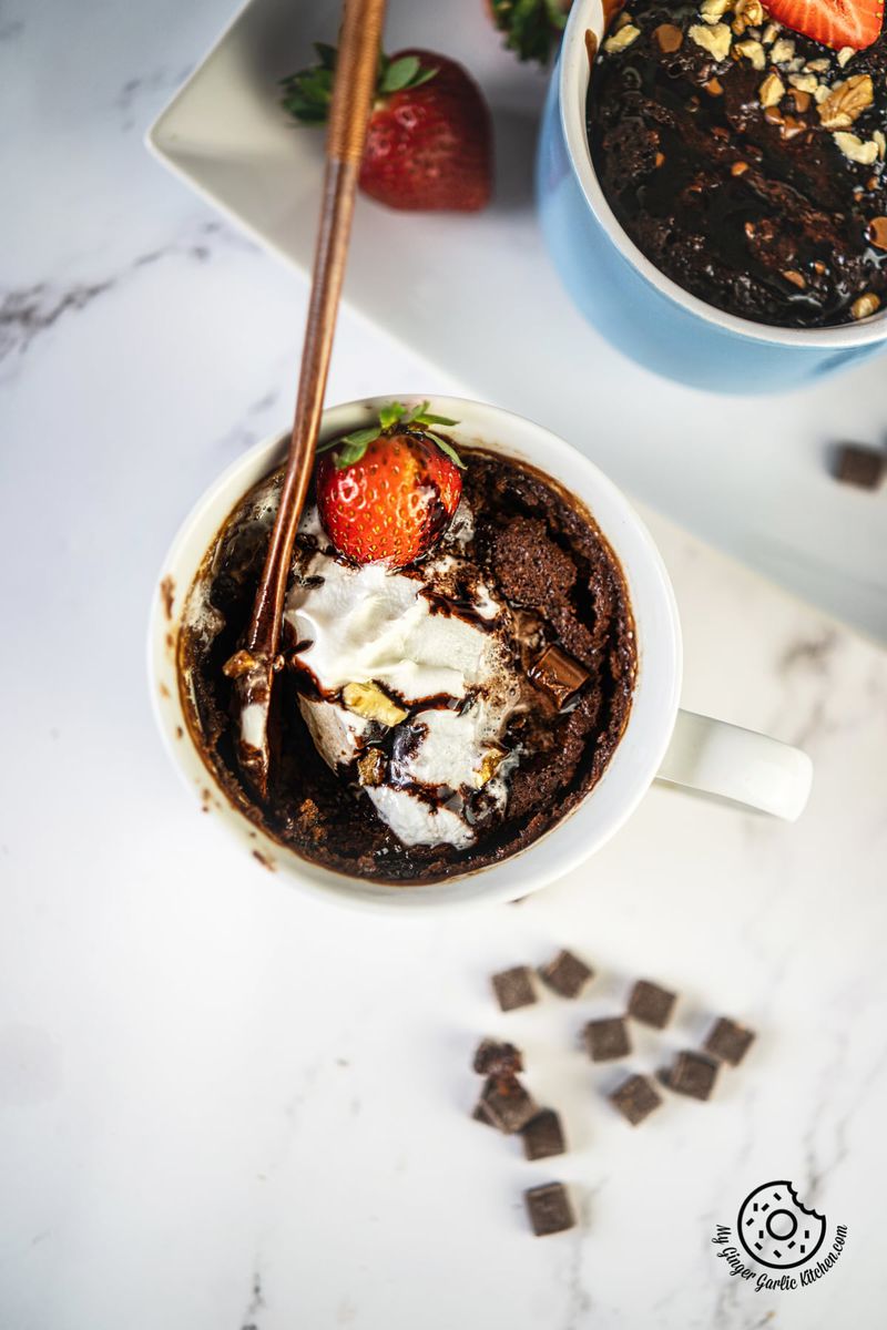 overhead shot of chocolate brownie in a white ceramic mug topped with whipped cream and strawberry