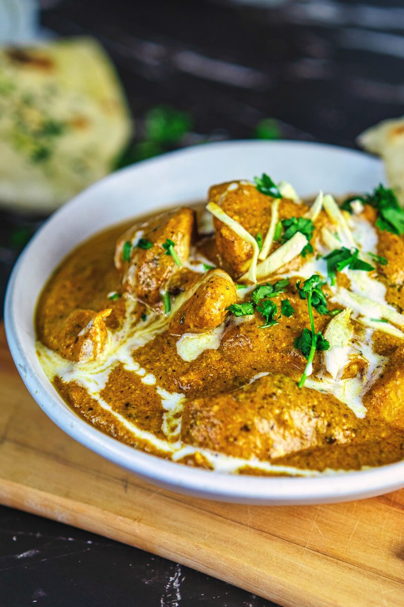 Close-up of butter chicken curry topped with cream and herbs, with a piece of naan on the side.