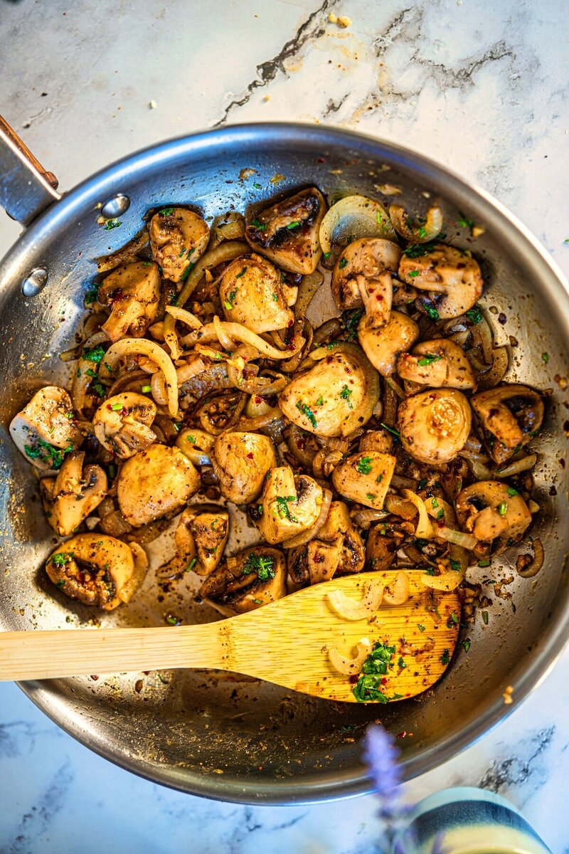 Butter garlic mushrooms sautéing in a skillet with onions, herbs, and golden caramelized edges