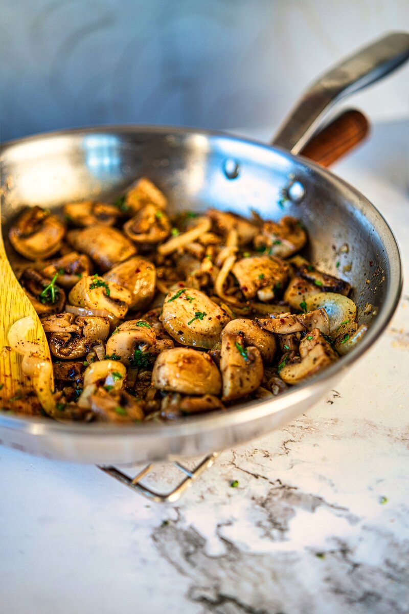 Butter garlic mushrooms cooking in a skillet with onions, herbs, and golden sautéed edges