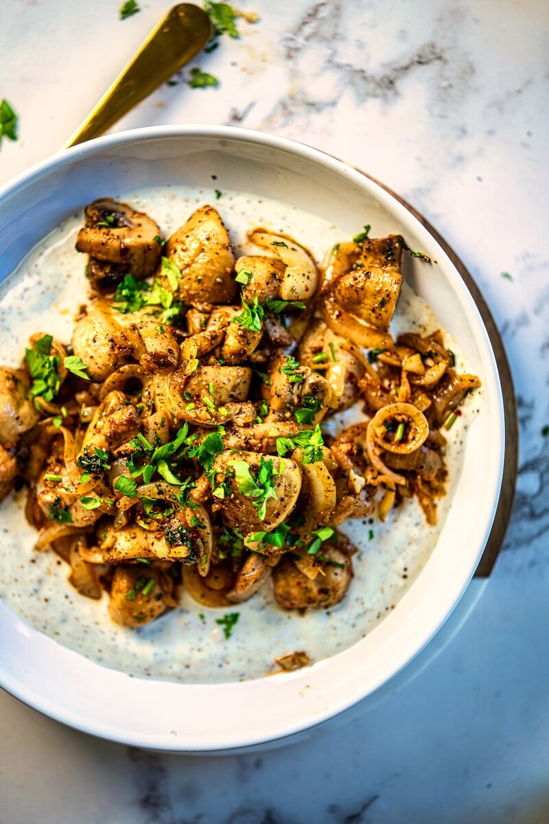 Garlic butter mushrooms served over creamy herbed yogurt sauce with fresh parsley garnish