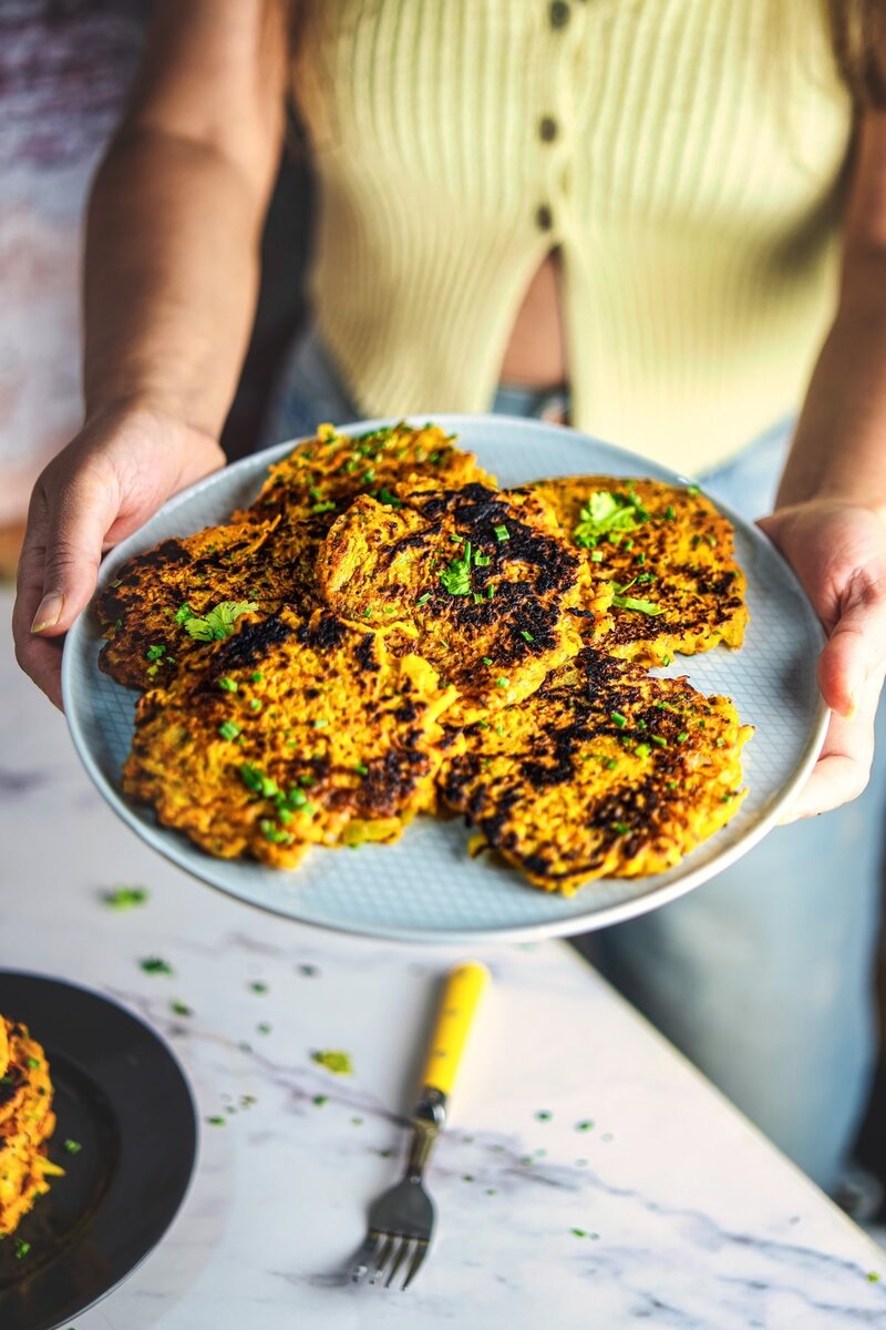 Butternut squash fritters on a green plate topped with herbs served beside mustard yogurt dip