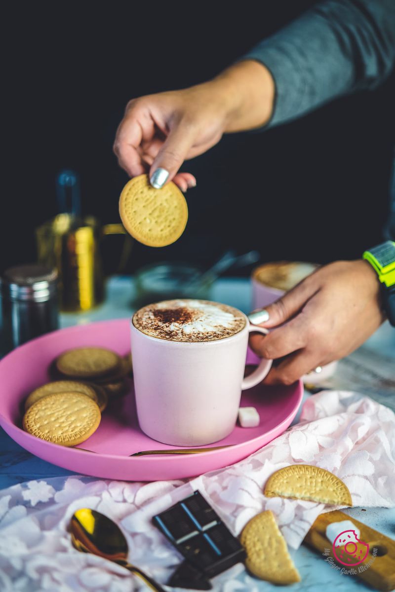 a woman holding biscuit over cafe mocha