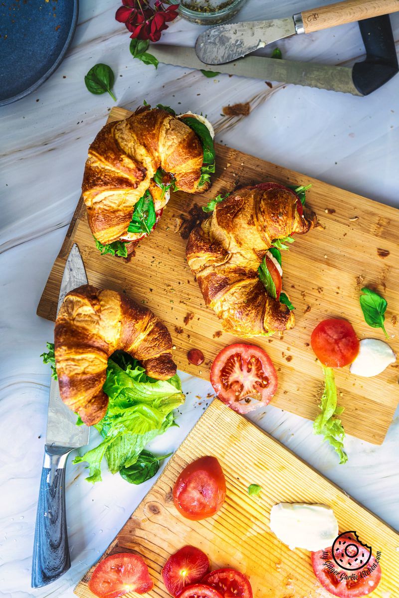 overhead shot of 3 mozzarella croissant sandwiches on a wooden board with tomato slices the side